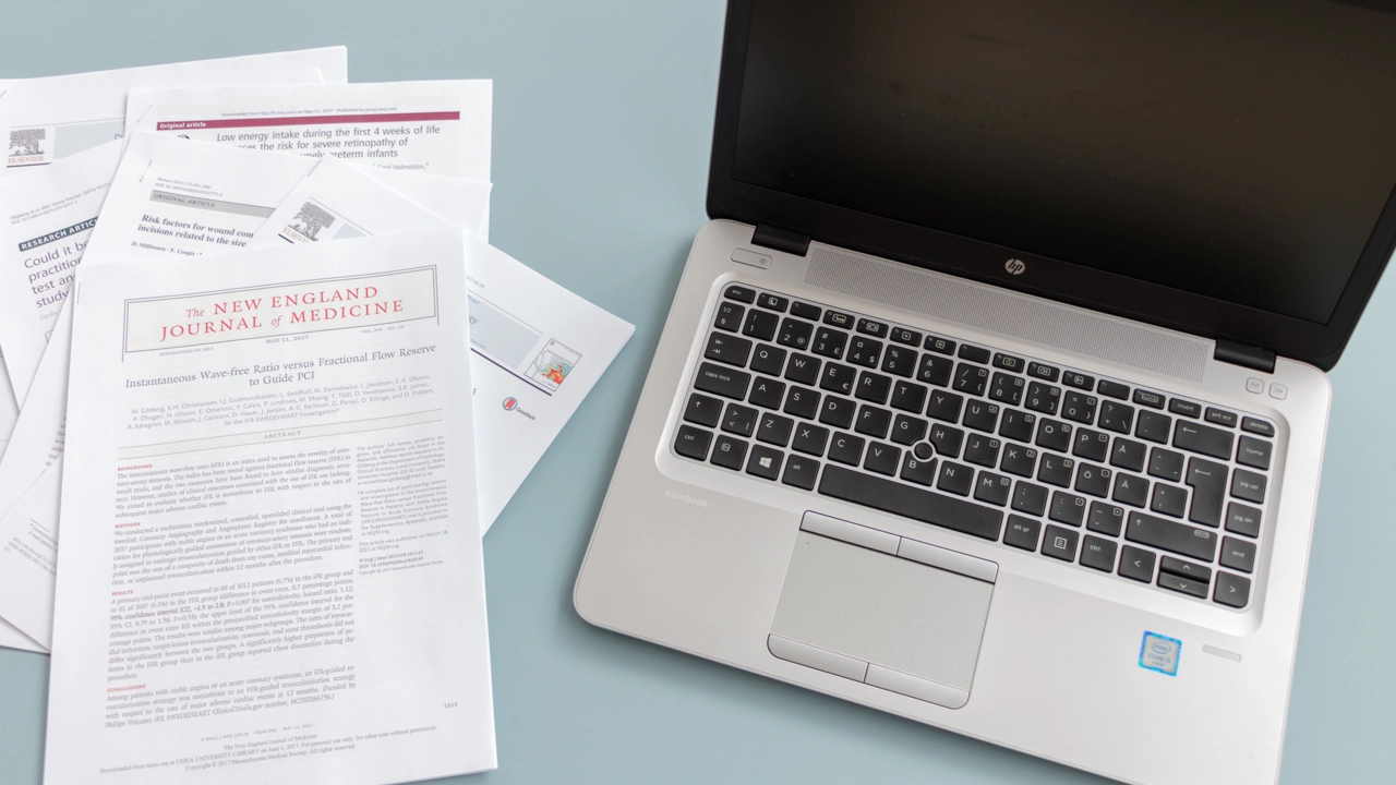 Några utskrivna artiklar ligger bredvid en bärbar dator. 