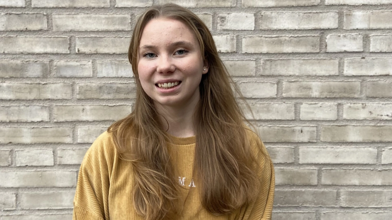 Porträttbild på Astrid Norstedt, beige tegelvägg i bakgrunden