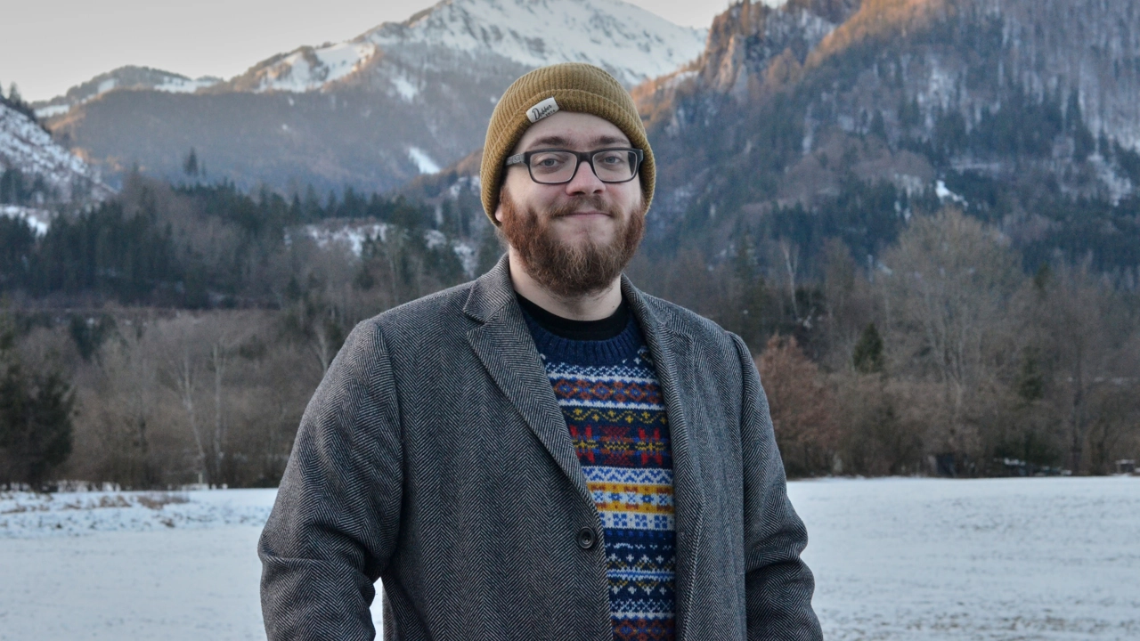 Bild på Bastian Schiffthaler stående utomhus, i bakgrunden sjö, skog och snöklädda berg