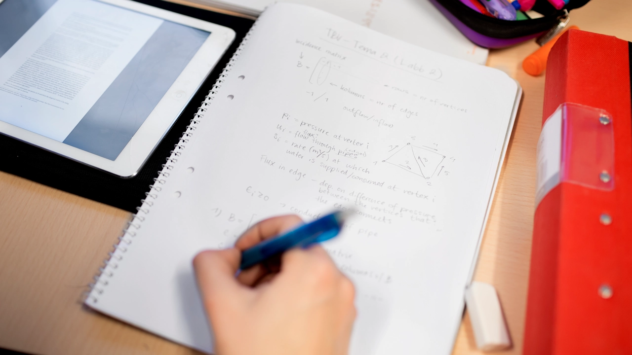 Bild på skrivblock med matematiktal och hand som håller i penna