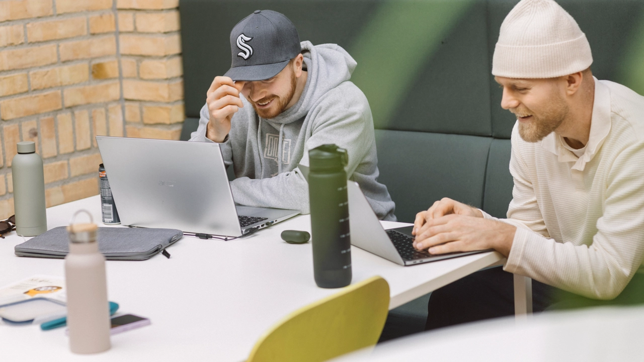 Två studenter sitter intensivt fokuserade på en skrivuppgift på en mysig studieplats på campus.