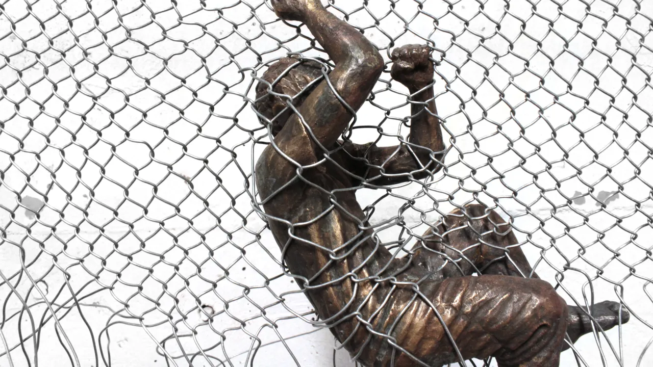 Bronsskulptur av person som sitter fast i ett nätstängsel