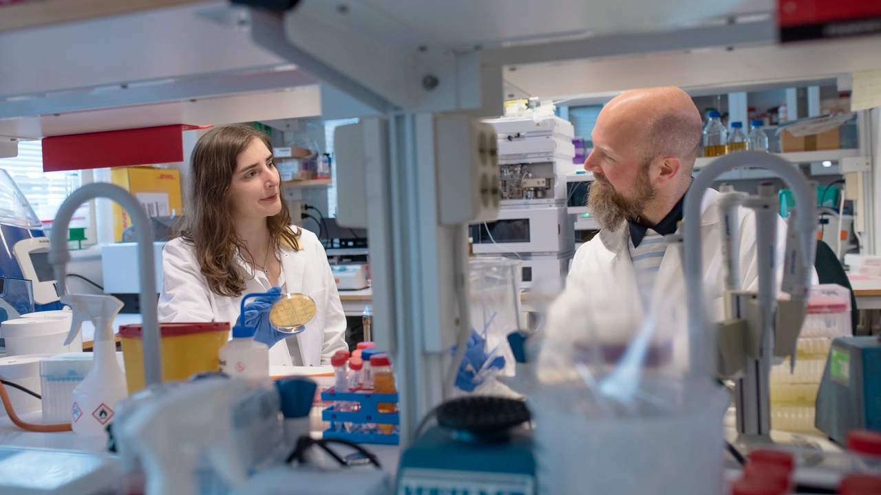 Två personer som syns på andra sidan av en hylla i ett labb.