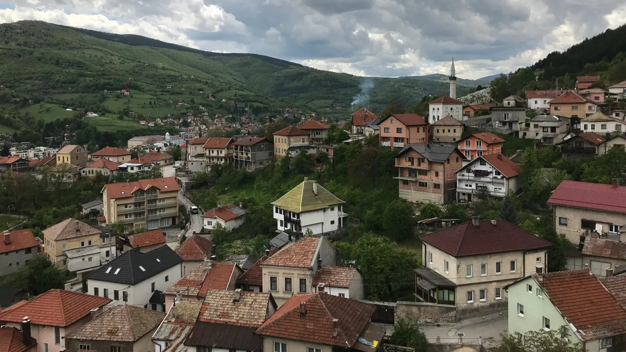 En by med hus i en dalgång i Bosnien. Skog och berg i bakgrunden.