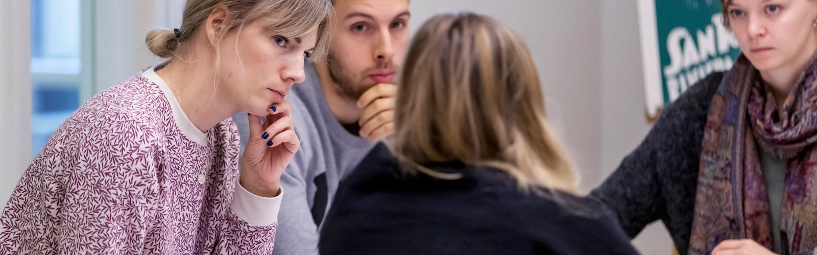 Fyra unga personer sitter runt ett bord. Tre lyssnar uppmärksamt på den fjärde.