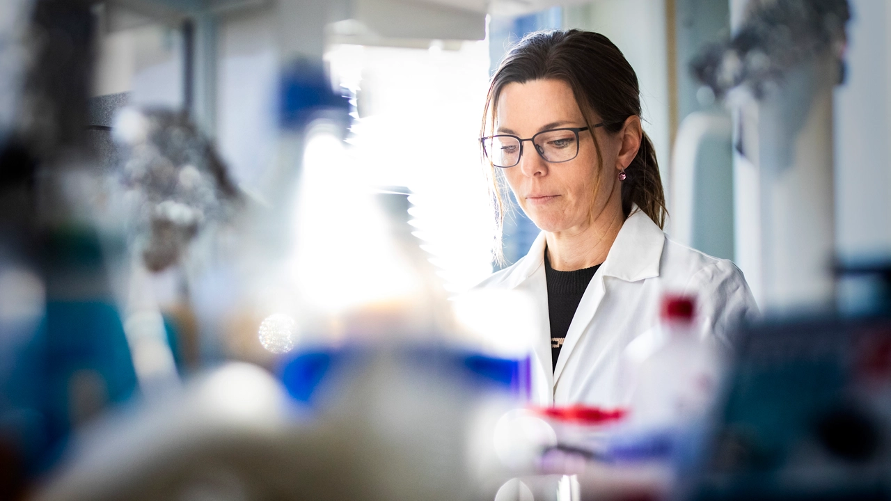 En kvinna i labbrock i fokus, i förgrunden suddiga instrument.