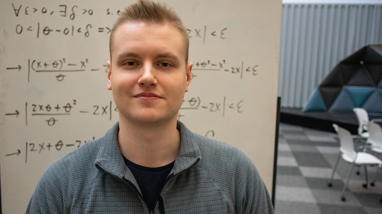 Porträttfoto på Christian Ekholm, i bakgrunde whiteboardtavla med matematiska formler