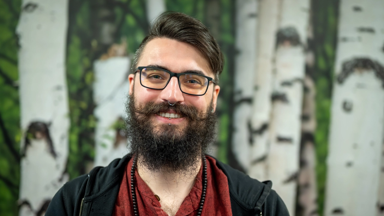 En man med skägg och glasögon framför en björk tapetbakgrund