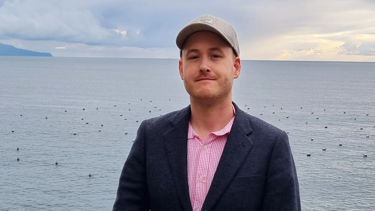 Man med kavaj och keps står framför ett hav.