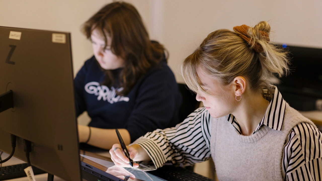 Two female students taking notes at a computer screen in a classroom.