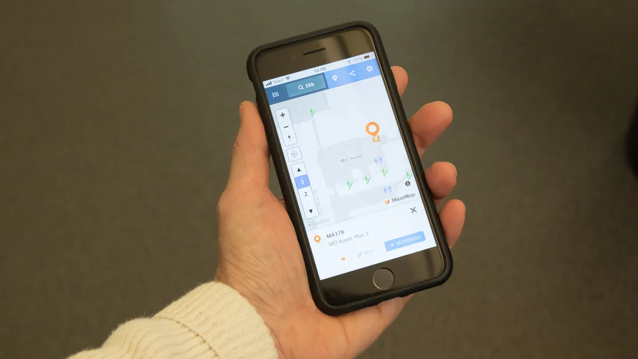 A hand holding a mobile phone showing the online map of campus.