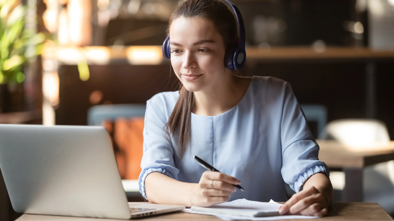 Kvinna som sitter och antecknar framför laptop.