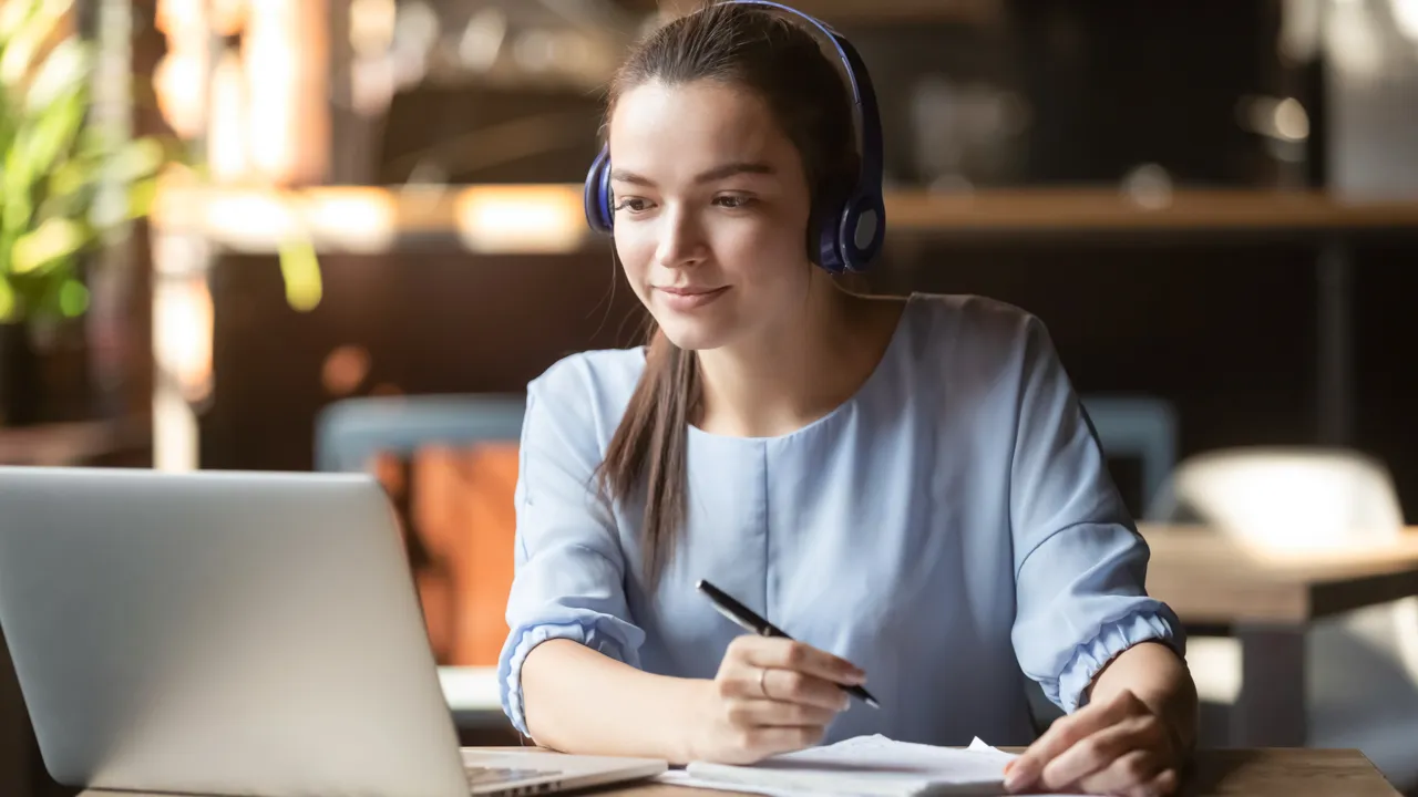 En kvinna som skriver anteckningar på ett papper från en datorskärm.