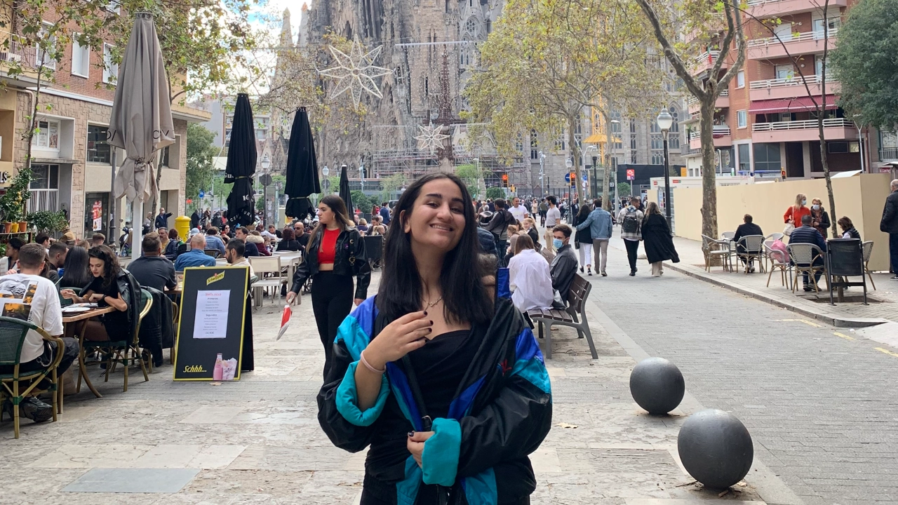 En av universitetets studenter blickar ut över en utländsk stad med färgglada byggnader och en flod.