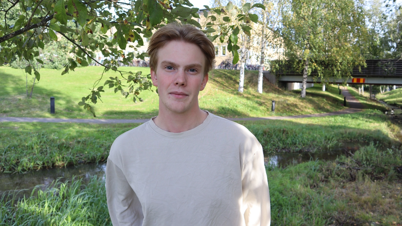 Porträttfoto på Edwin Gustafssson, i bakgrunden träd och buskar på campus