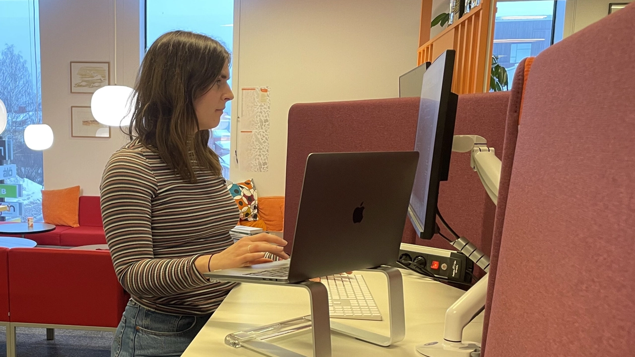 Elin Lindén stående vid sin arbetsplats i kontorslandskapet på Ecogain