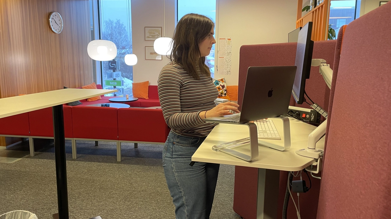Photo of Elin Lindén standing i front of the computer at her desk