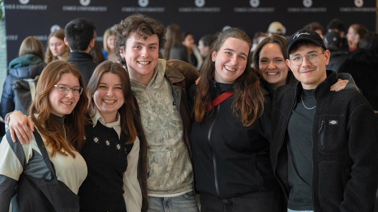 Smiling students holding each other over the shoulders in a row.