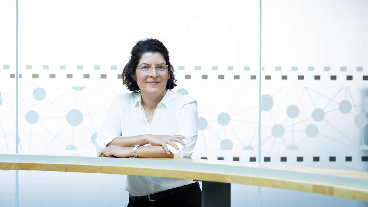 A woman stands behind a wooden railing with her arms crossed.