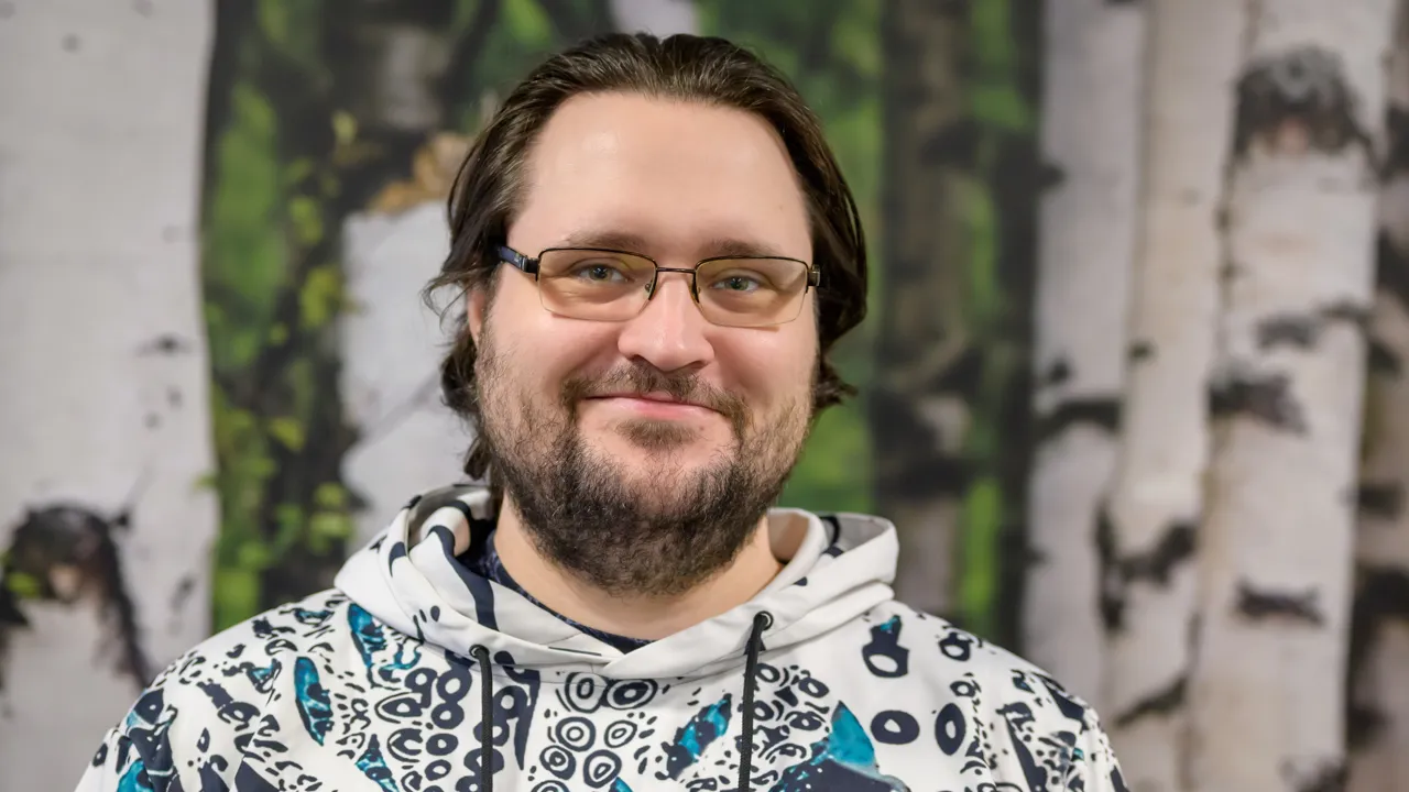 A head and shoulders portrait of Florian Albrecht who is wearing a white hoodie with marine motifs, against a backdrop of white birch forest wallpaper