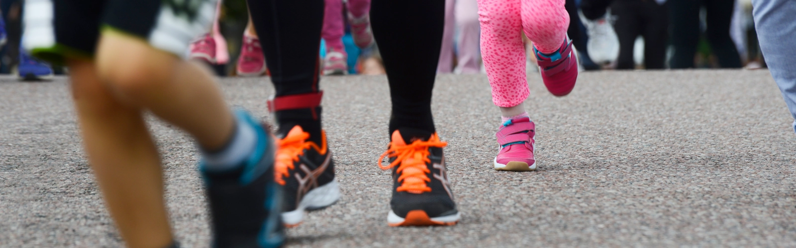 Fötter på personer i olika åldrar som springer på asfalt.