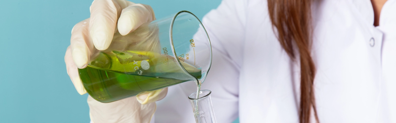 Kvinnlig kemist i vit rock  som häller en lösning i ett provrör.