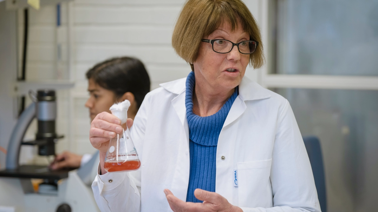 Två kvinnor i vita labbrockar som arbetar i laboratoriemiljö. 