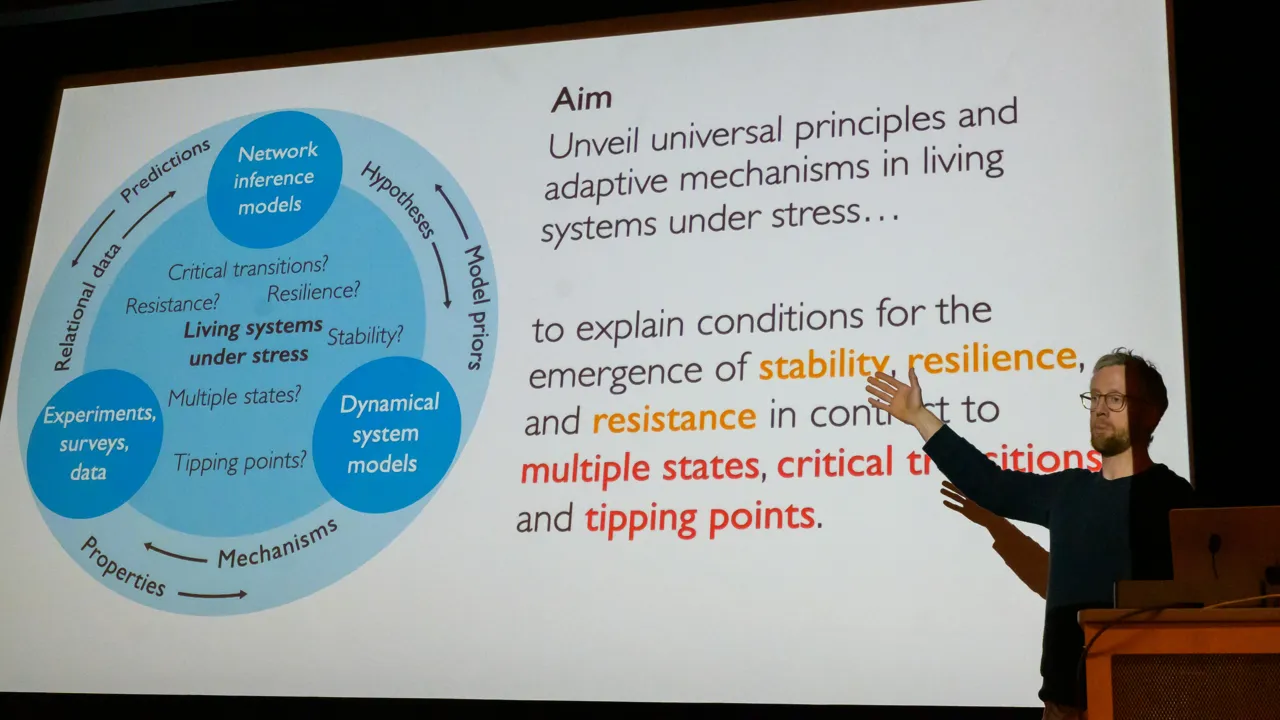 Martin Rosvall står vid sidan av en stor skärm på vilken en bild visas med bilder och text som beskriver stressresponsmodellering vid IceLab