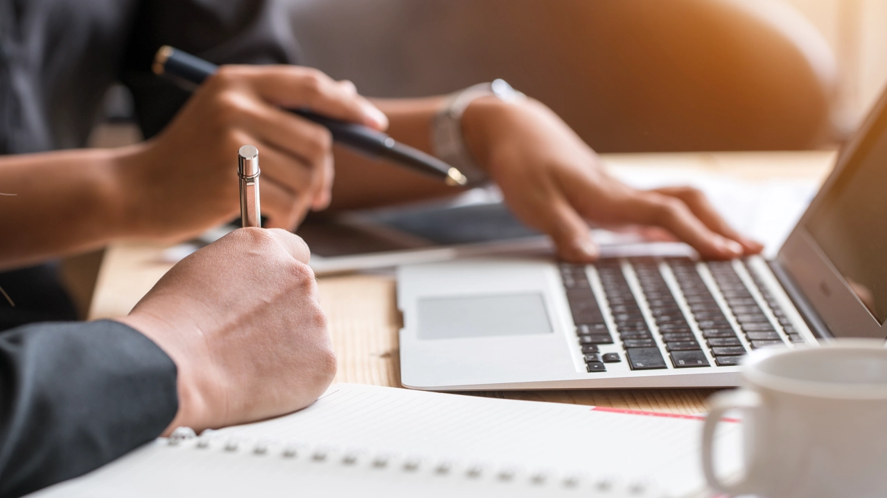 Händer från två personer som samarbetar framför dator. 