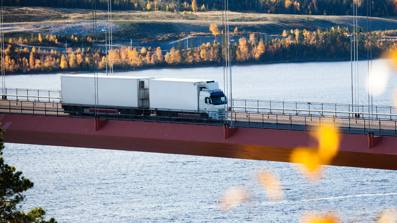 En långtradare kör över Höga kusten-bron genom ett landskap av höstfärger. 