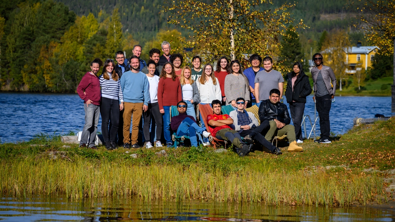 Människor som står i ett höstlandskap vid en flod.