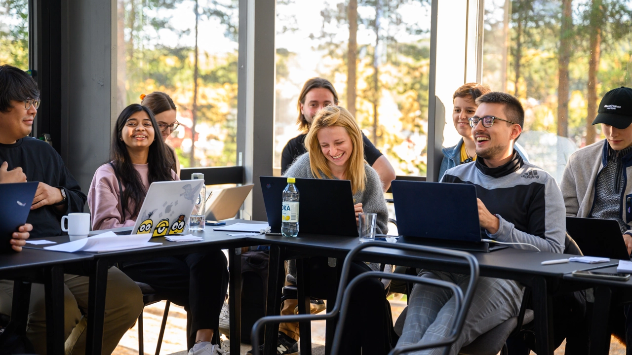 A group of people sitting around a table with laptops