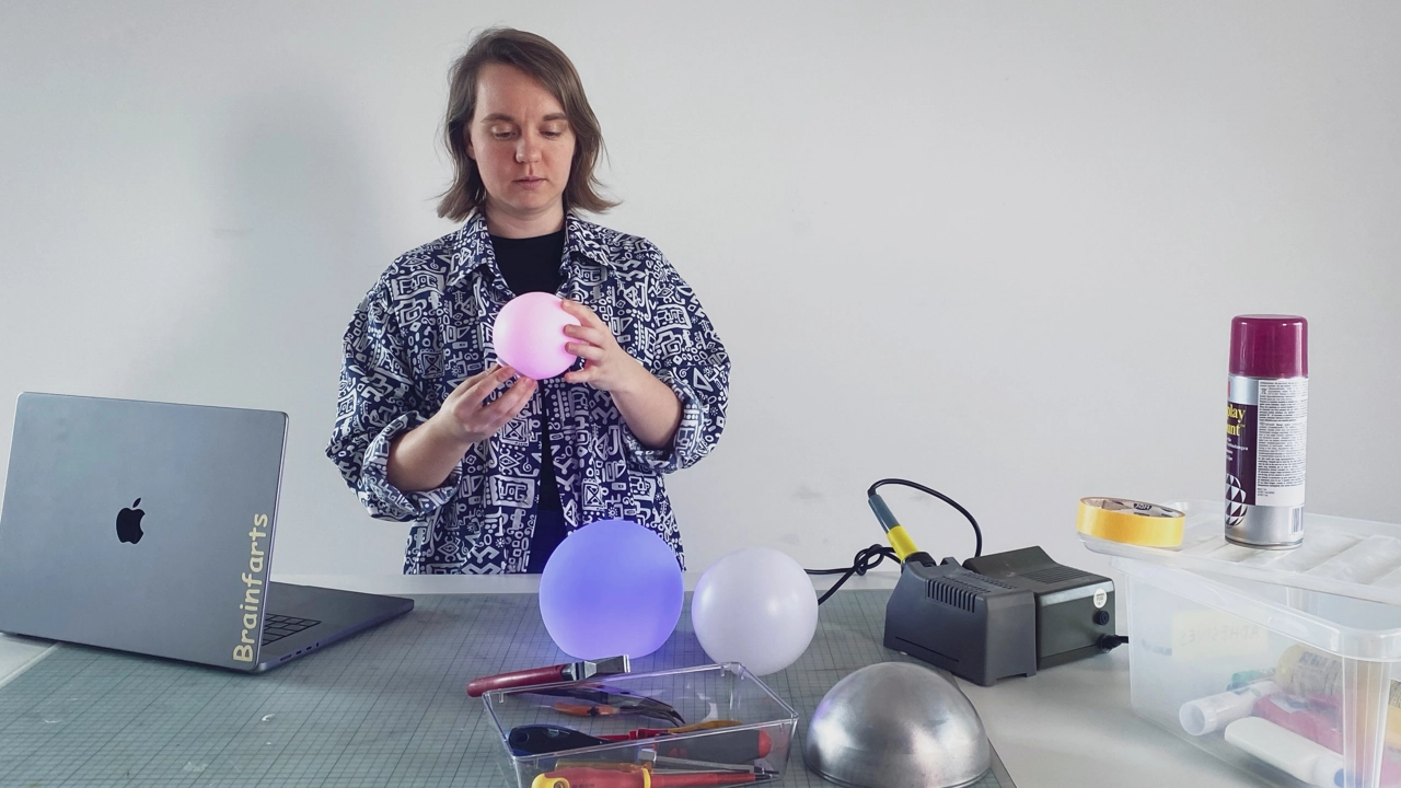 Bild på Ilse Pouwels vid sitt arbetsbord, håller i en rosa ballong