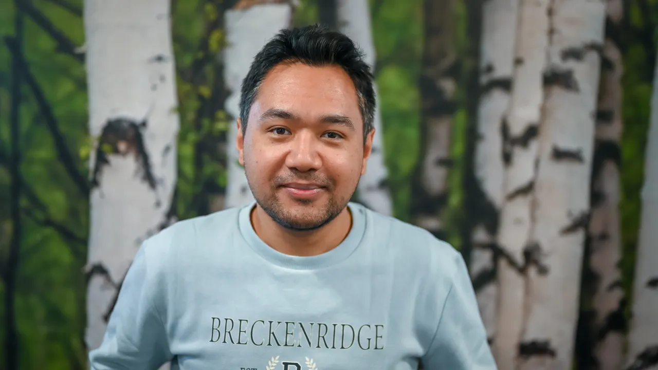 A portrait of a man in front of a wallpaper of birch trees