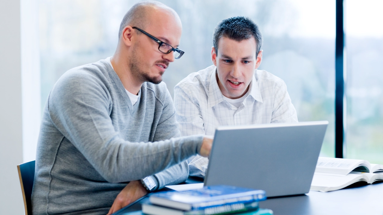 Två män sitter vid ett bord och tittar på en bärbar dator.