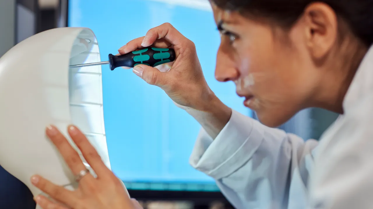 A woman is screwing on a robot-like construction with a screwdriver.