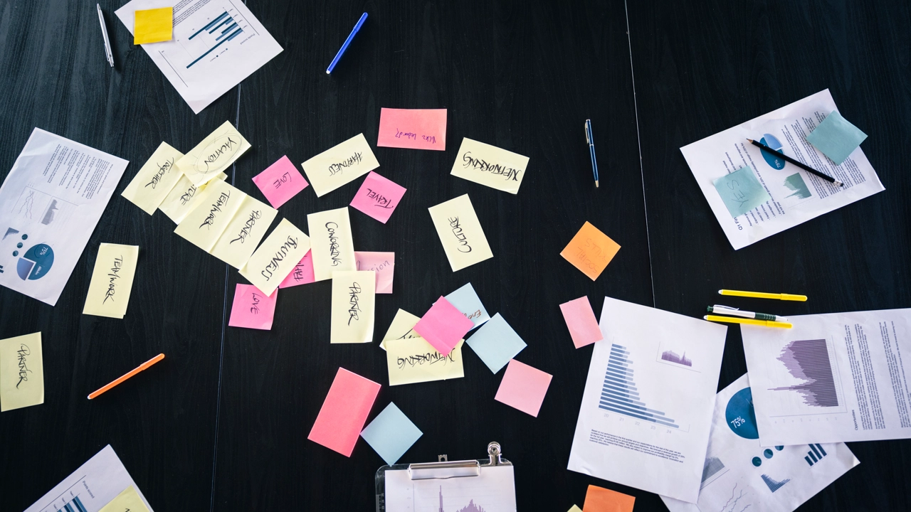 Papper och notislappar ligger utströdda över en svart yta.