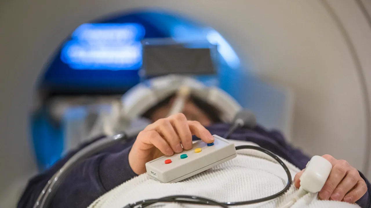 En person ligger med handen på en fjärrkontroll på en brits för en magnetkameraundersökning.