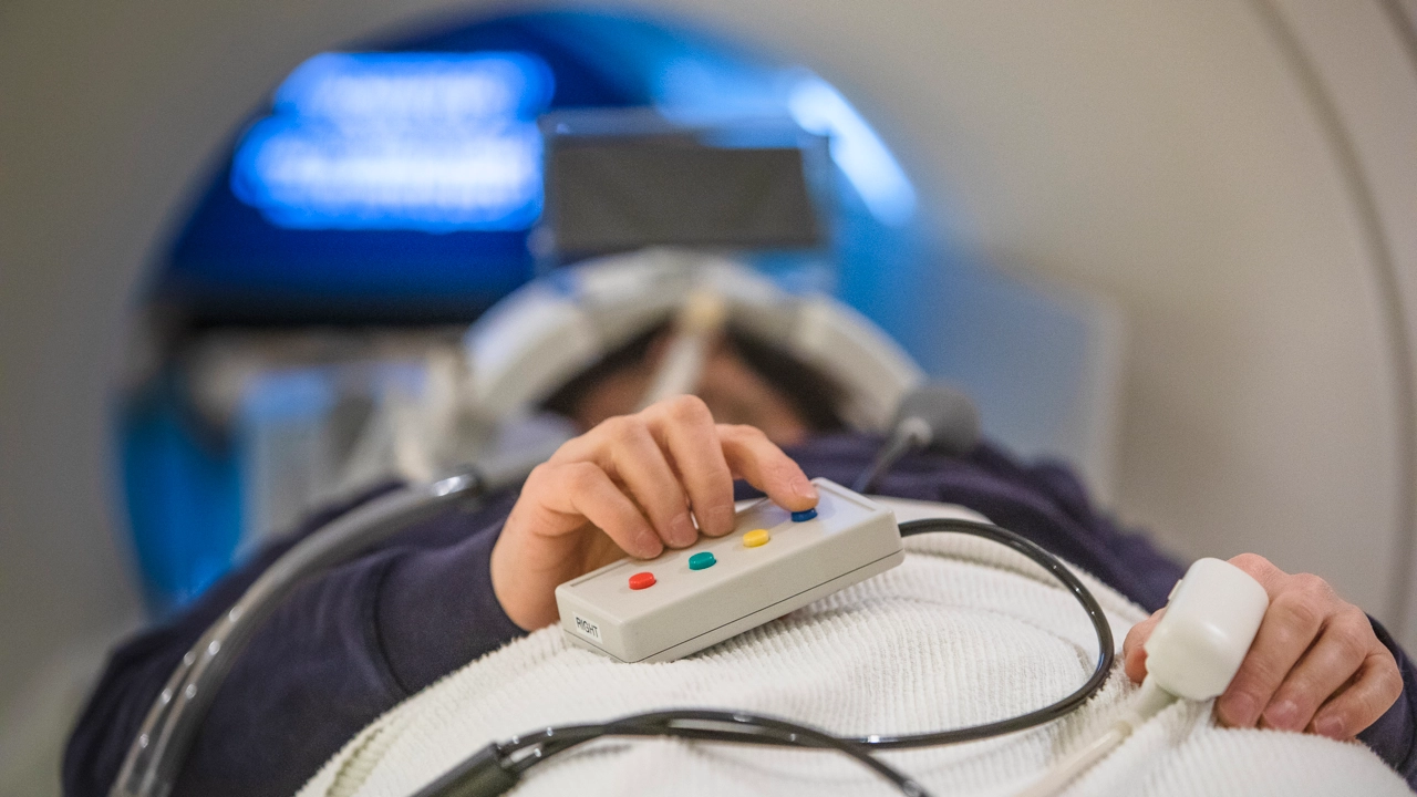 A person is lying on a table for an MRI scan with their hand on a remote control.