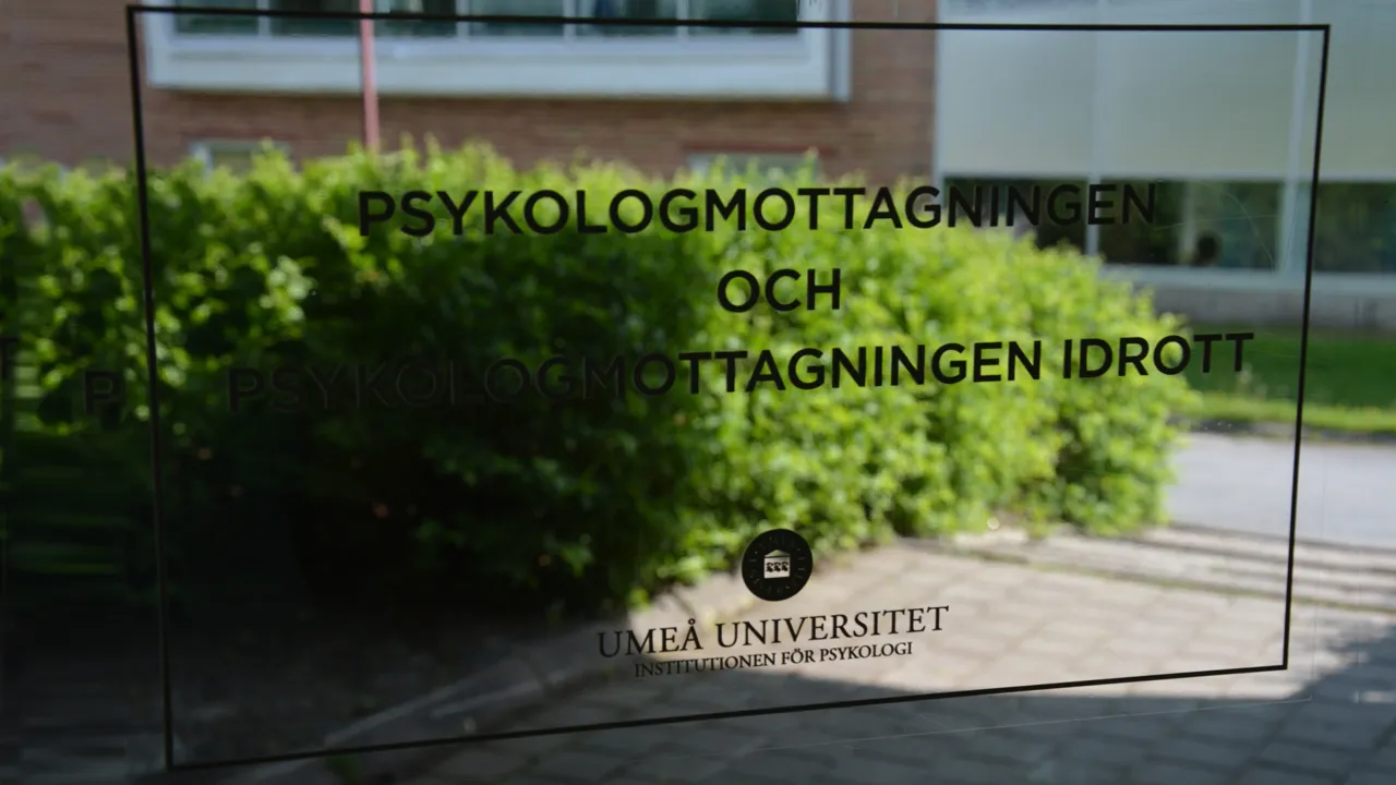 Foto taget från Psykologmottagningens glasdörr ut mot en grön häck. Text på glaset anger Psykologmottagningen.