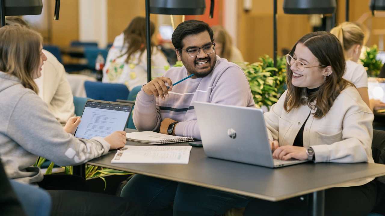 Three students in conversation over a group work in a cosy study space on campus.