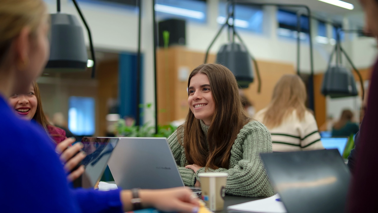 A happy student is interacting with others in a cosy study space.