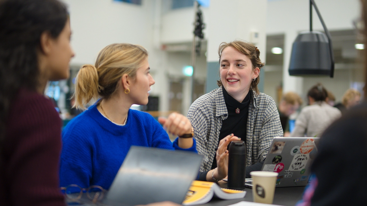 Tre studenter samtalar vid sina datorer.