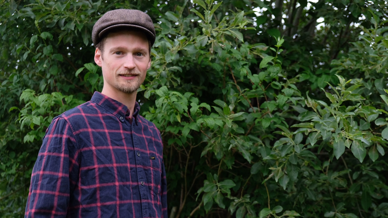 Man med hatt framför en stor buske