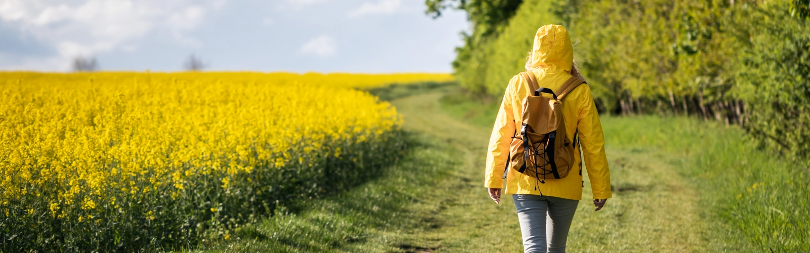 Kvinna med ryggsäck promenerar intill ett rapsfält.