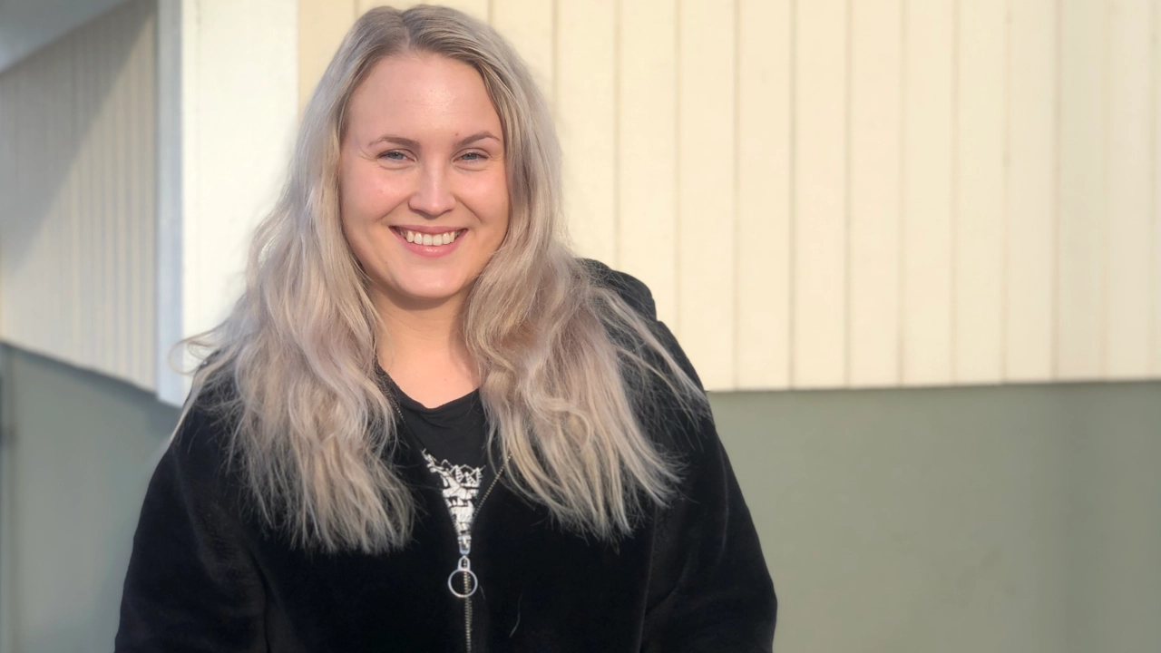 Bild på Izze Niemi, i bakgrunden en träfasad