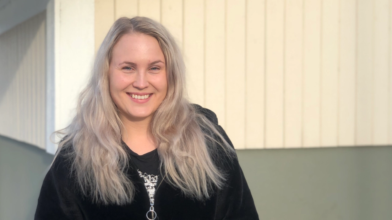 Bild på Izze Niemi, i bakgrunden gul träfasad