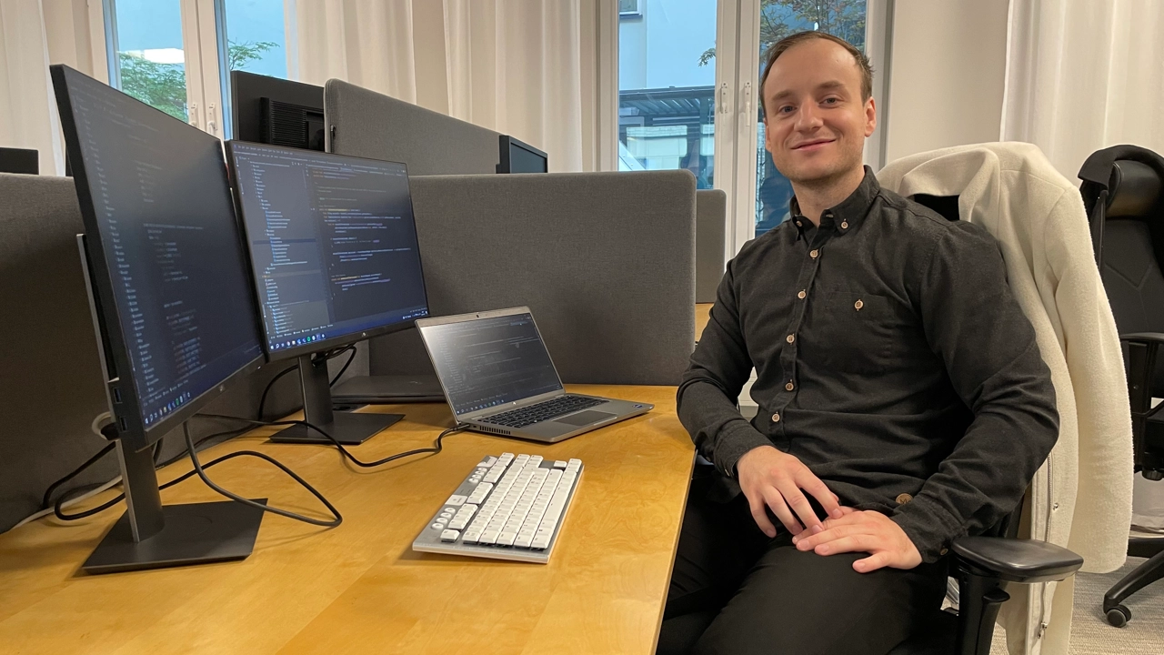 Bild på Jakub Jagiello sittande vid skrivbord omgiven av datorskärmar