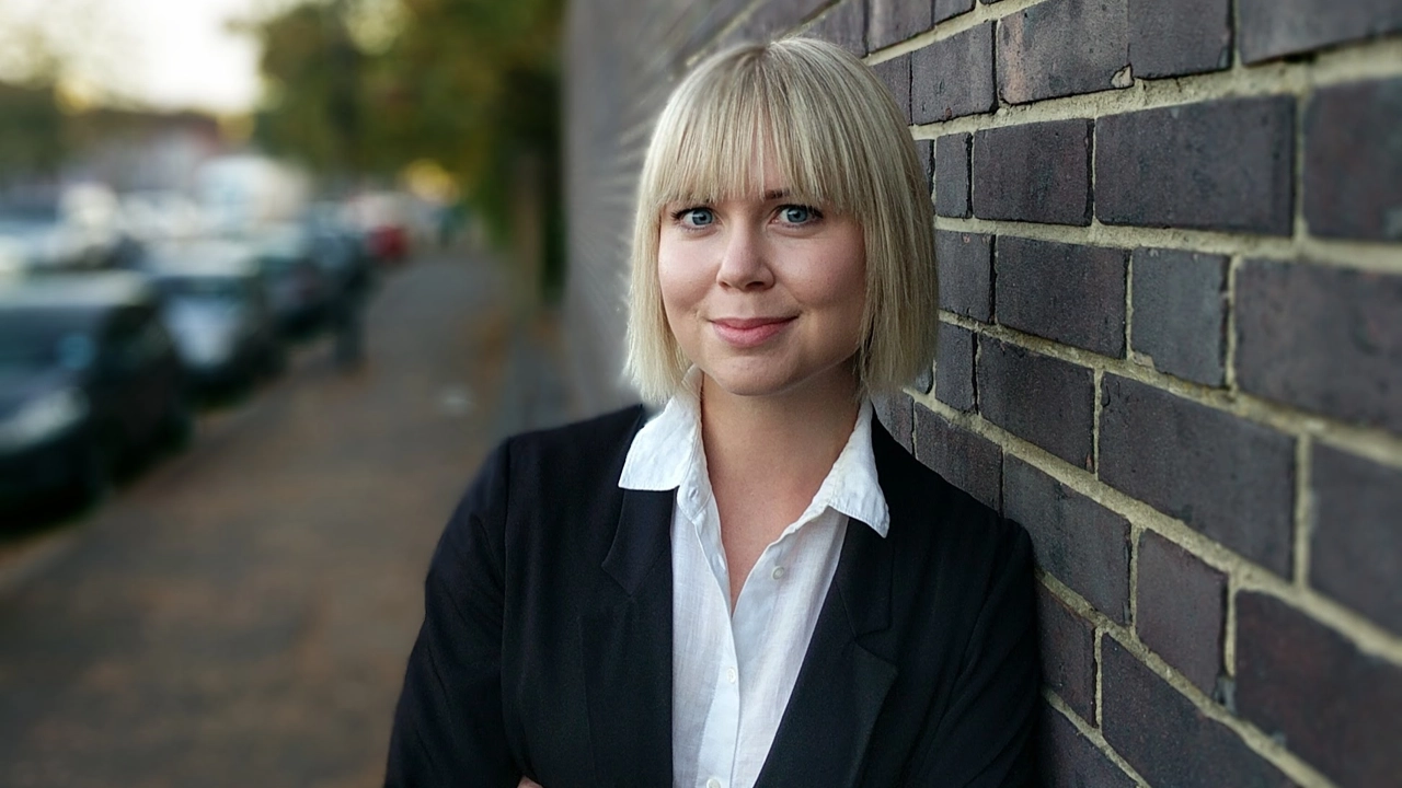 Porträttfoto av Jennifer Eriksson, i bakgrunden gata och mörk tegelvägg