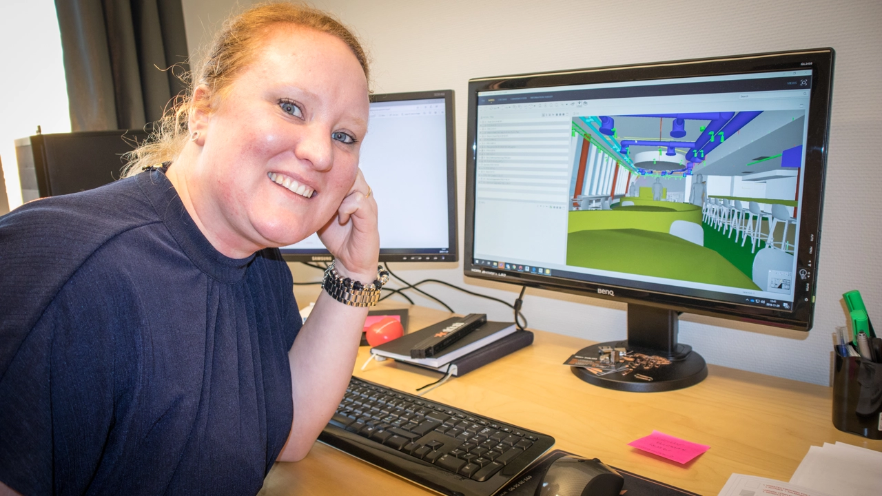 Bild på Jenny Öhrling vid skrivbordet, i bakgrunden datorskärmar